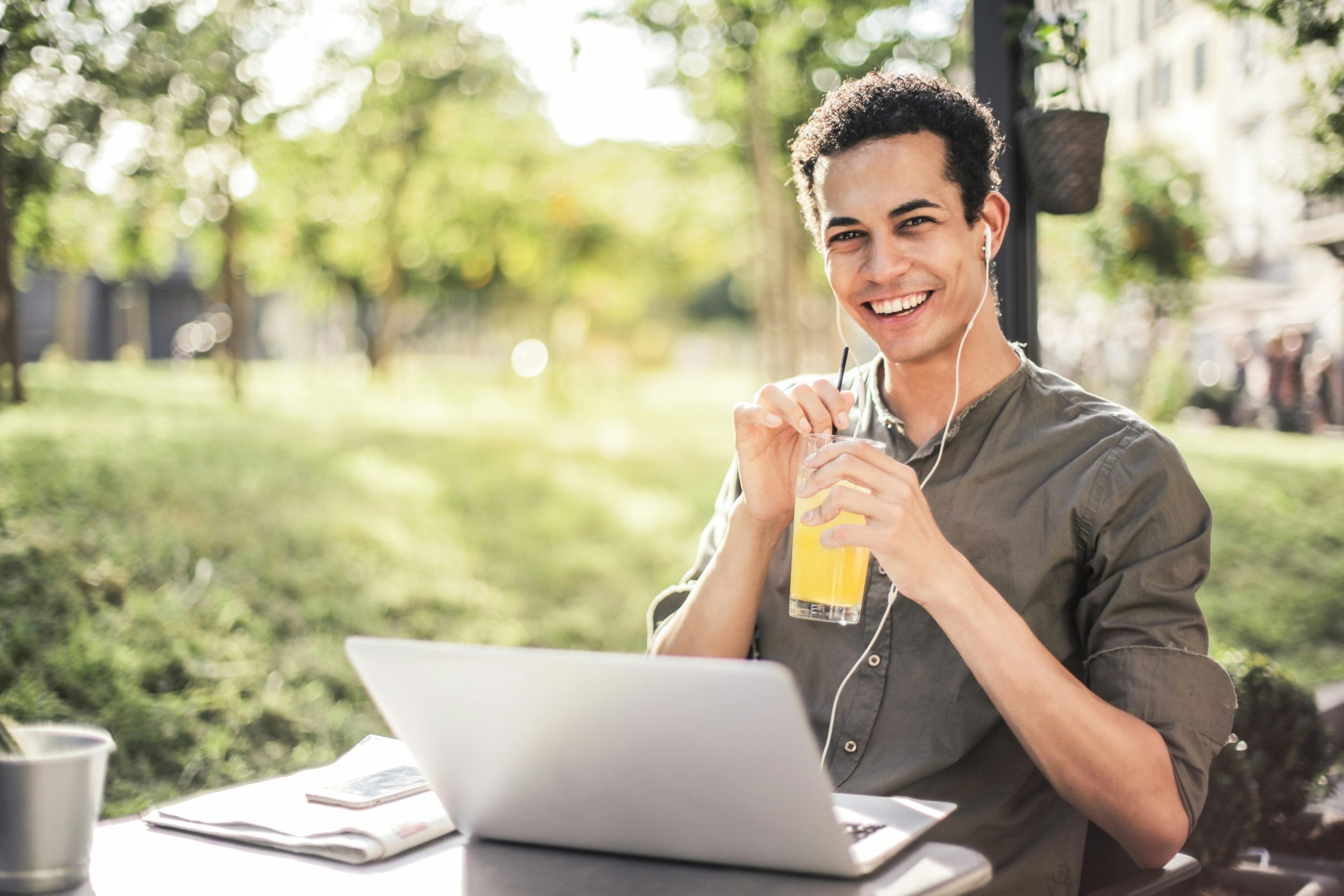  A happy man sitting with a laptop and a glass of juice in a park. 