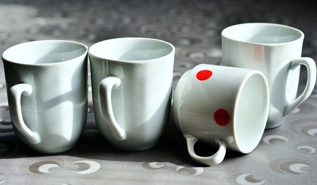 Four porcelain mugs with one of them having 2 red dots and being on the ground.