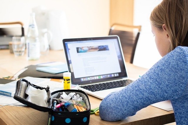 A girl sitting in front of her laptop with a pencilcase and a glue stick next to her.