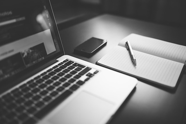 A laptop iphone, and a notebook with a pen on desk.