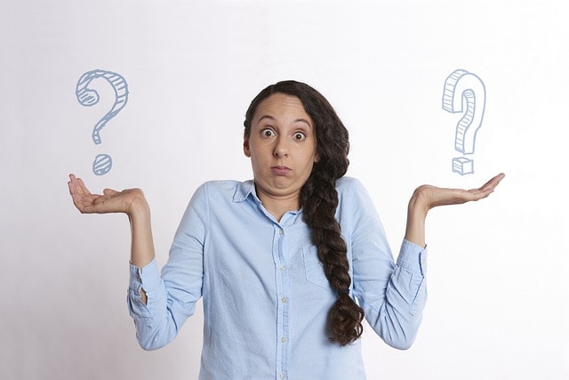 A woman holding two question marks and looking confused.