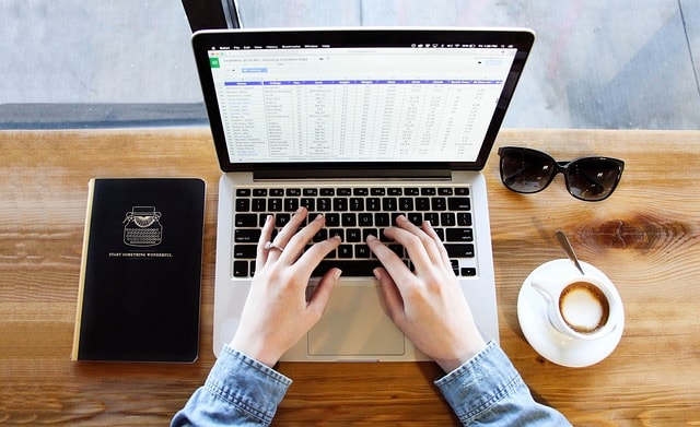 A person typing on a laptop with a cup of coffee and notebook next to them.