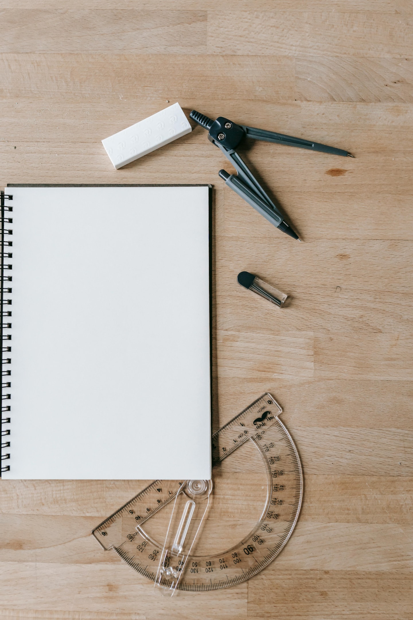 Geometry utensils and a notebook placed on top of a wooden desk. 