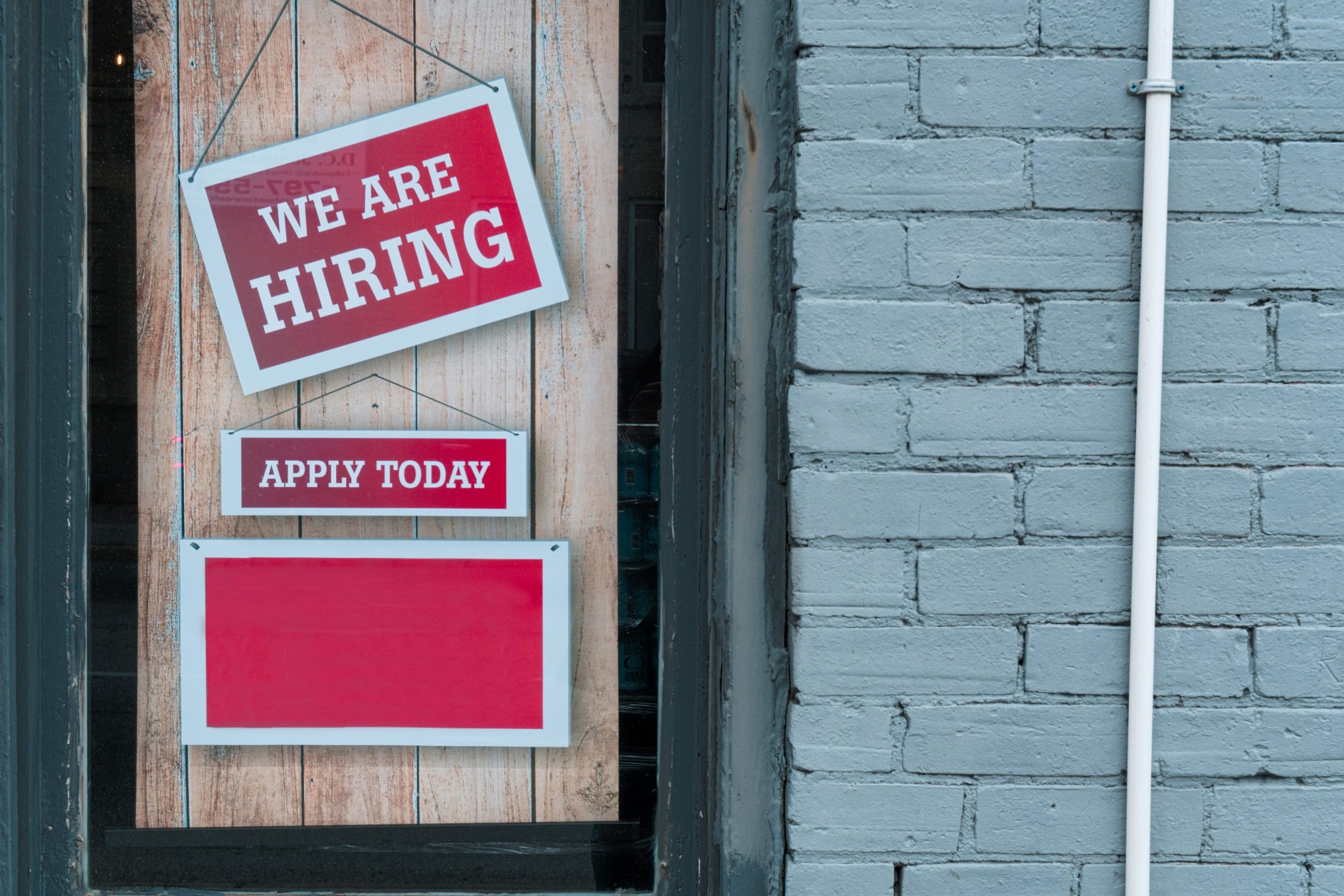 A wooden door next to a grey wall with a red sign that says "We are hiring."