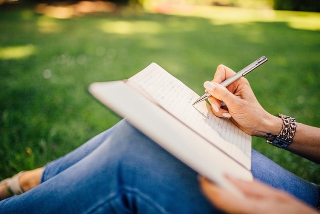 A woman on blue jeans writing notes in a notebook.