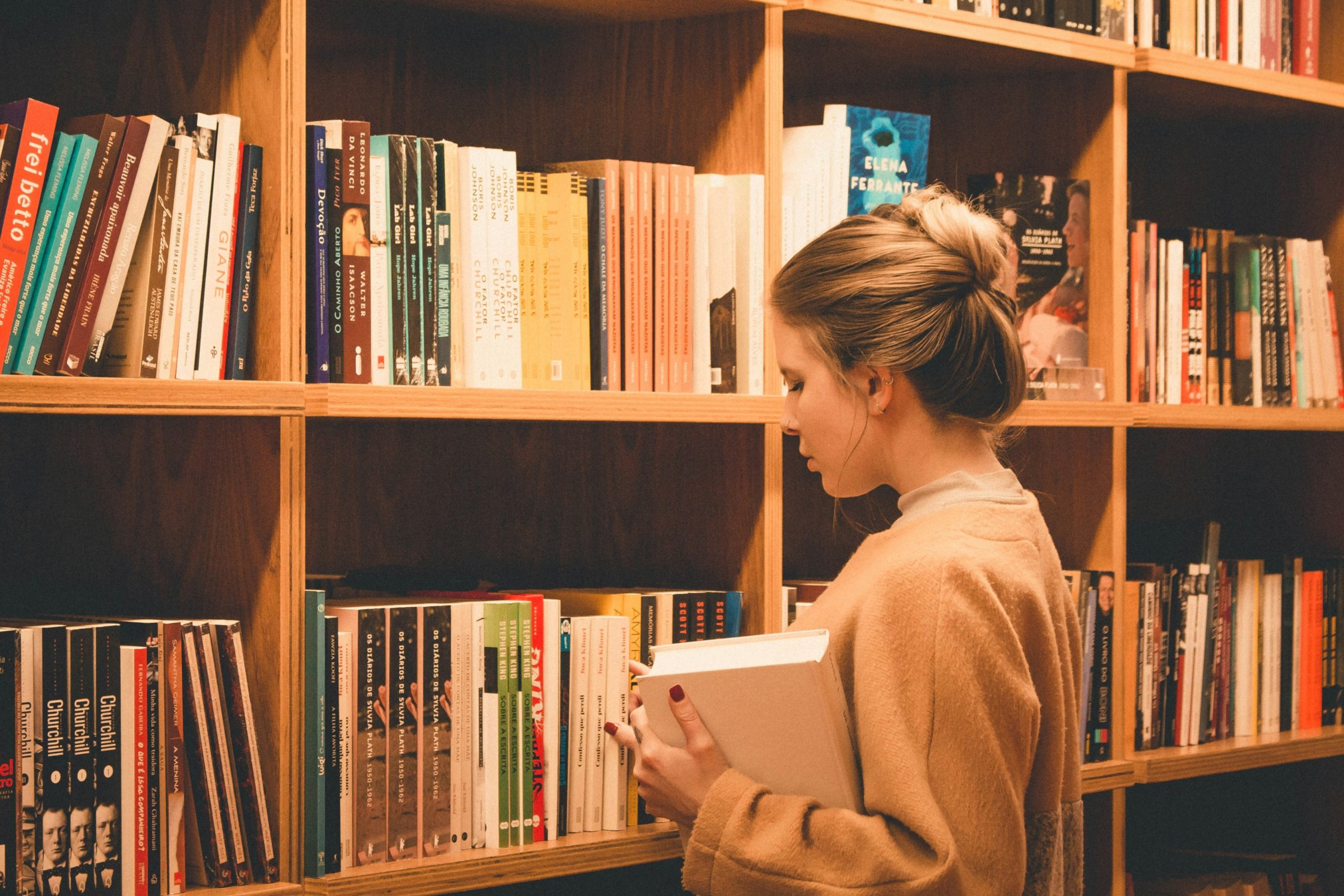 A woman picking up books from a library shelf.