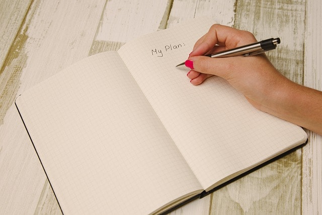 A person writing in a notebook where the top of the page has the word "Plan."