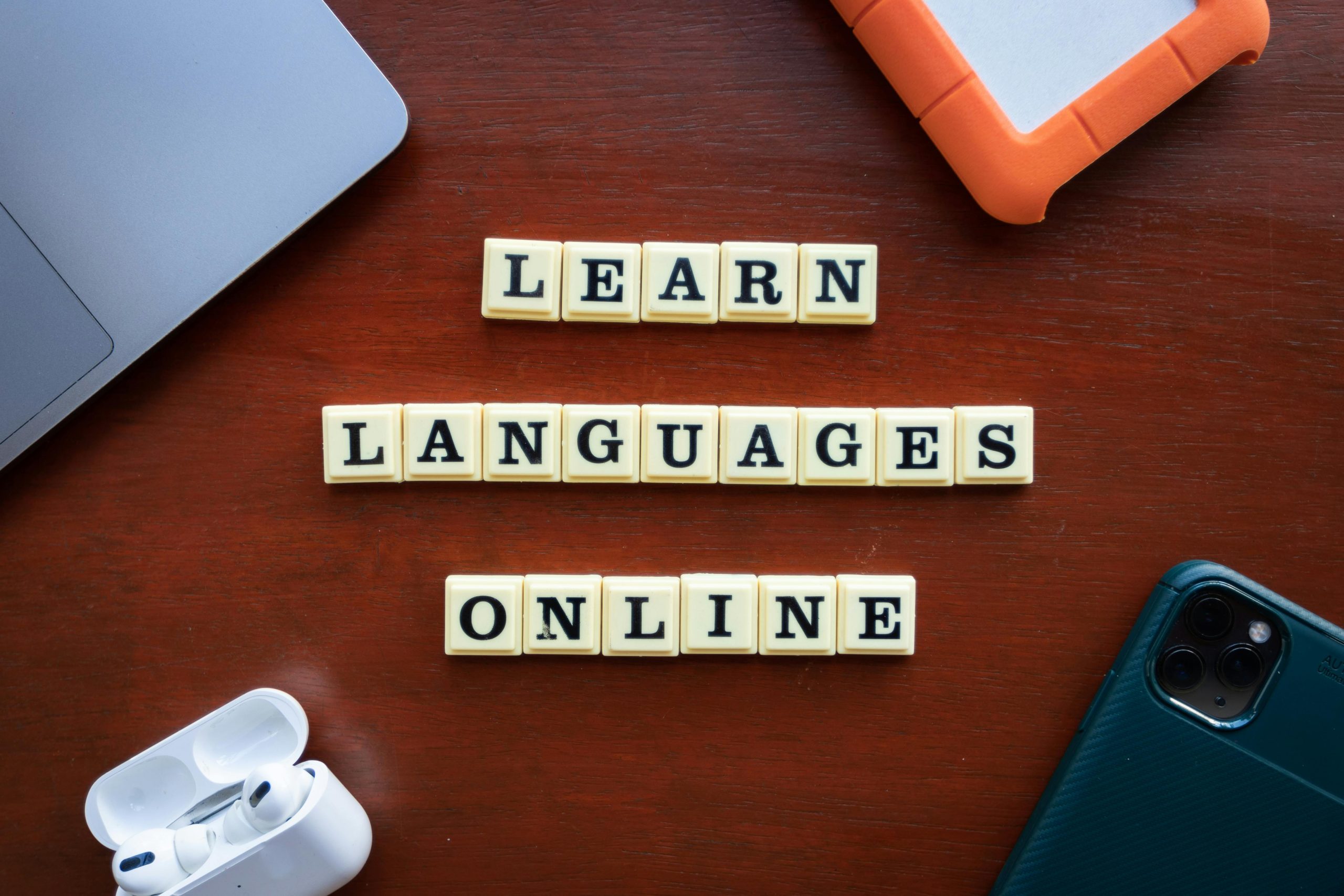 Scrabble tiles next to a phone and earpods spelling the phrase "learn languages online."