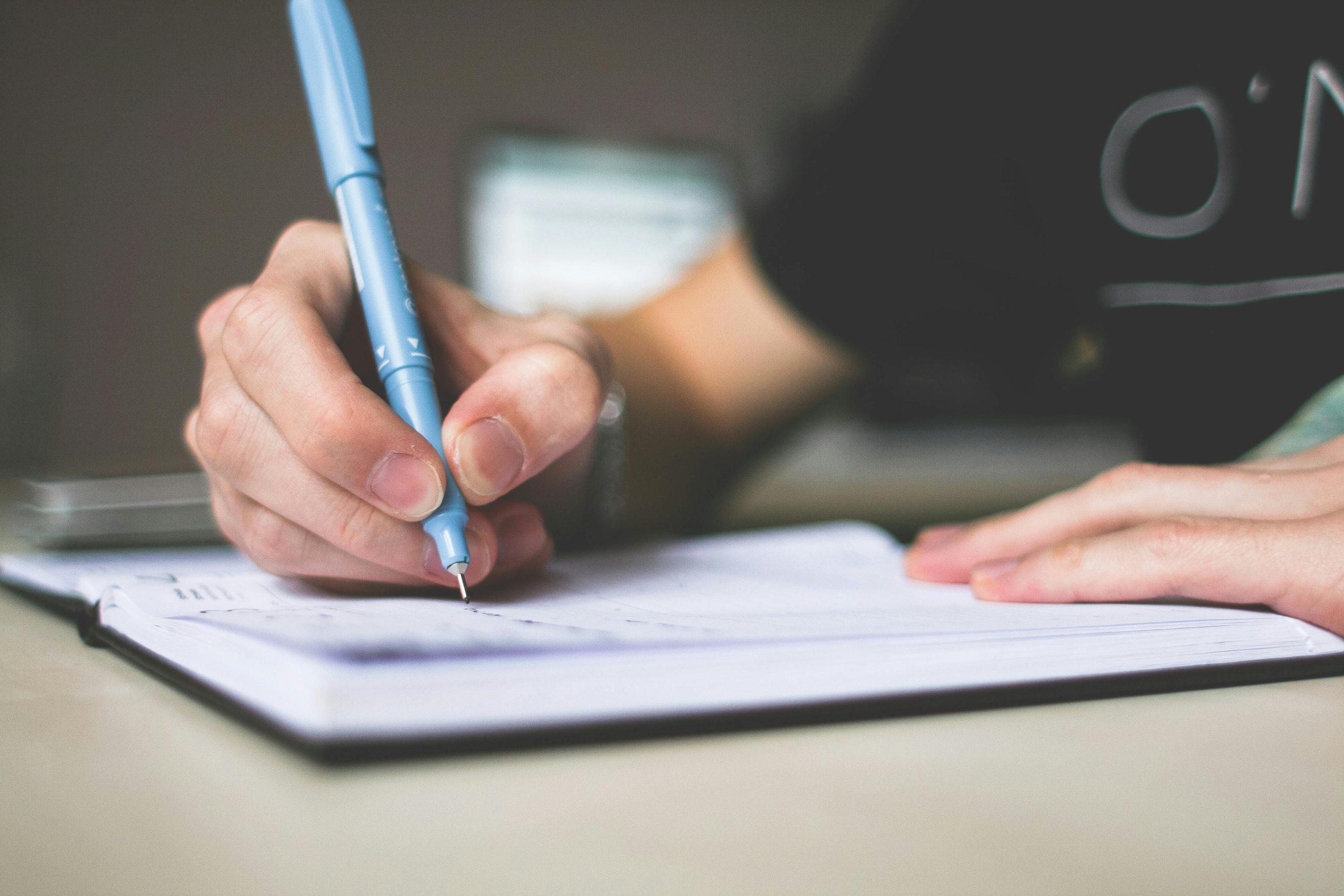 A person writing on a piece of paper with a blue pen. 