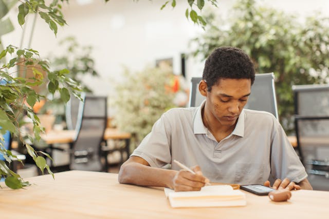 A student writing an essay and reading text from his phone. 