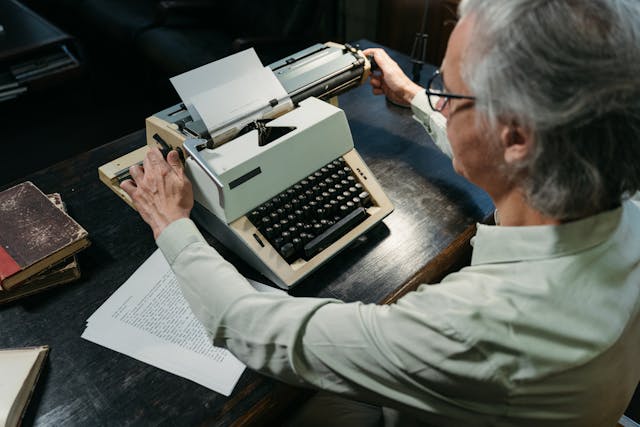 A man sitting at a typewriter writing an essay.
