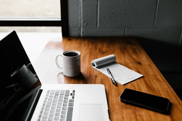 A notepad and coffee on a desk next to a computer. 