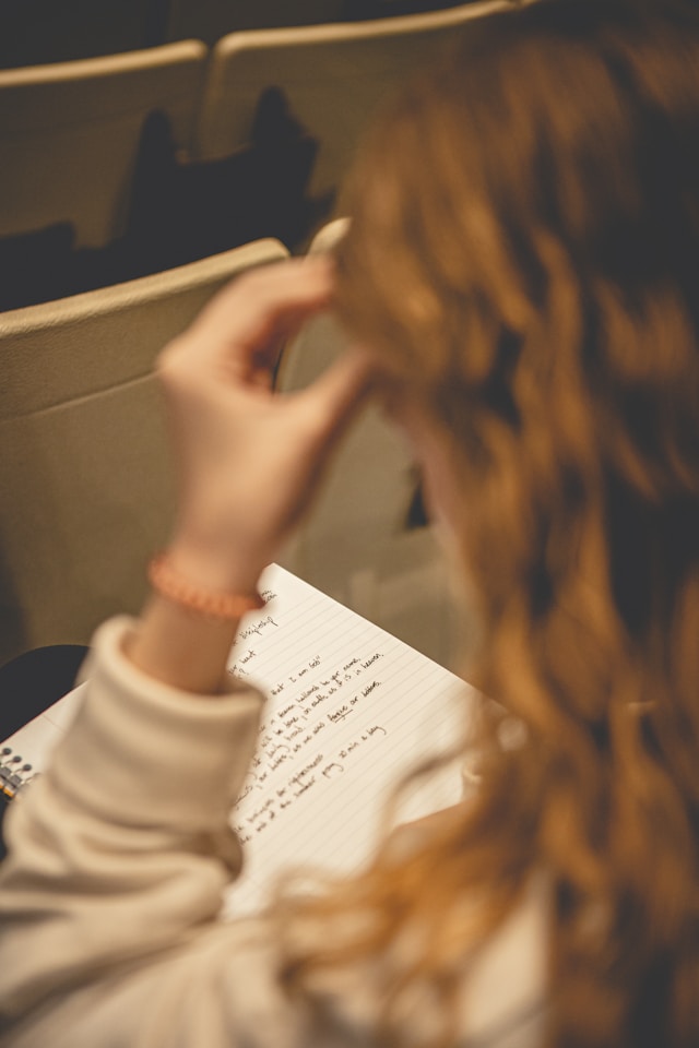 A woman with a yellow sweater looks at an open notebook. 