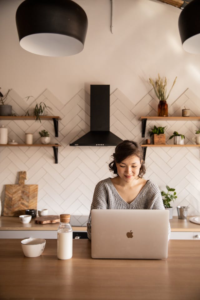 A smiling woman using a laptop in a modern kitchen. 