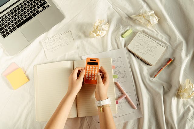  A person using a calculator, sitting next to pieces of paper with math on them. 