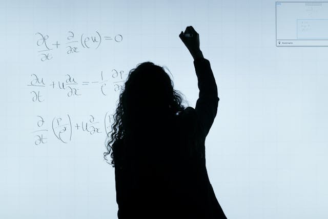 A silhouette of a woman writing math equations on a whiteboard. 