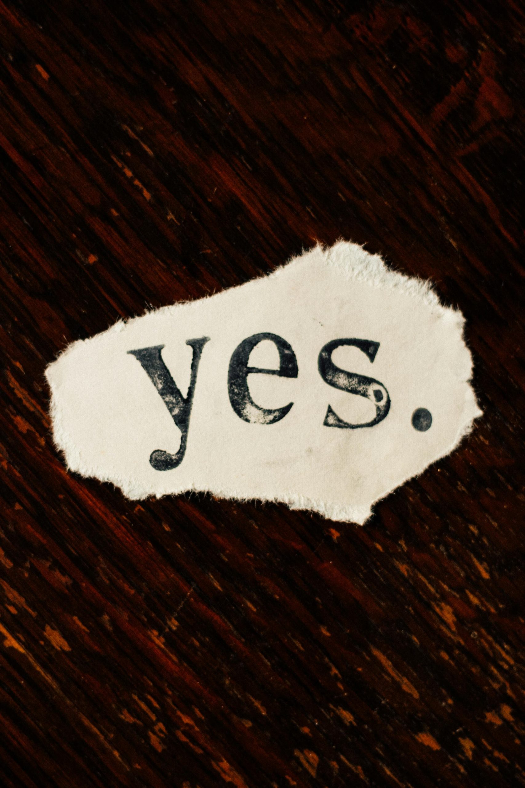 A close-up of a piece of paper with yes in black font on a brown wooden surface. 