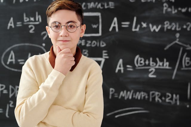 A person with a yellow sweater stands in front of a blackboard with a math equation. 