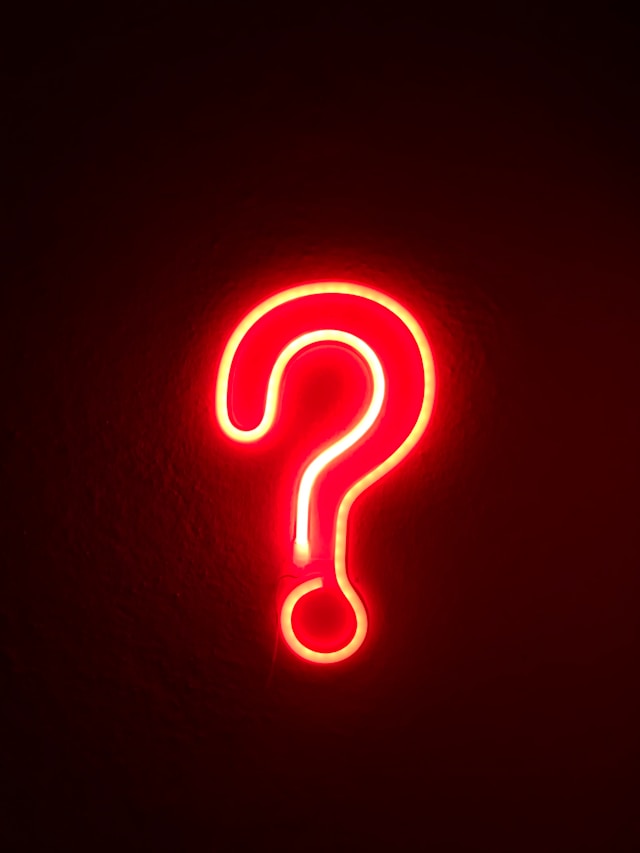 A close-up of a neon red question mark on a wall. 