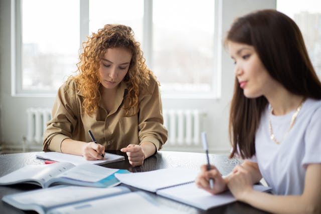 Two young women writing notes for their essays in notebooks. 