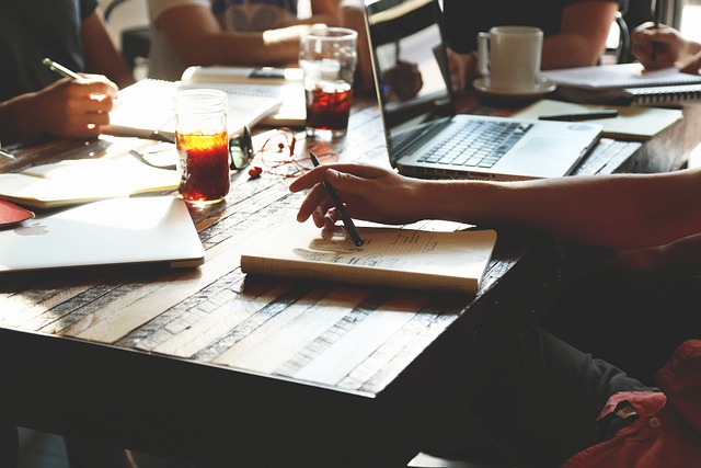 A group of people sitting at a table with their laptops and notebooks out. 