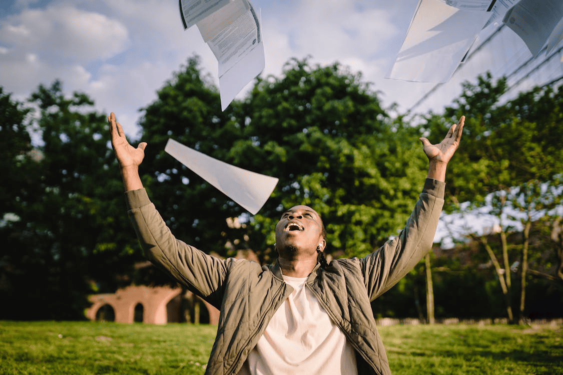 Young man happily throwing papers in the air to symbolize a lack of stress thanks to the use of AI graders.