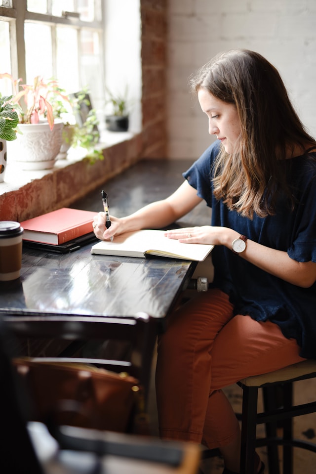 A woman sitting in a coffee shop writing in a journal. 