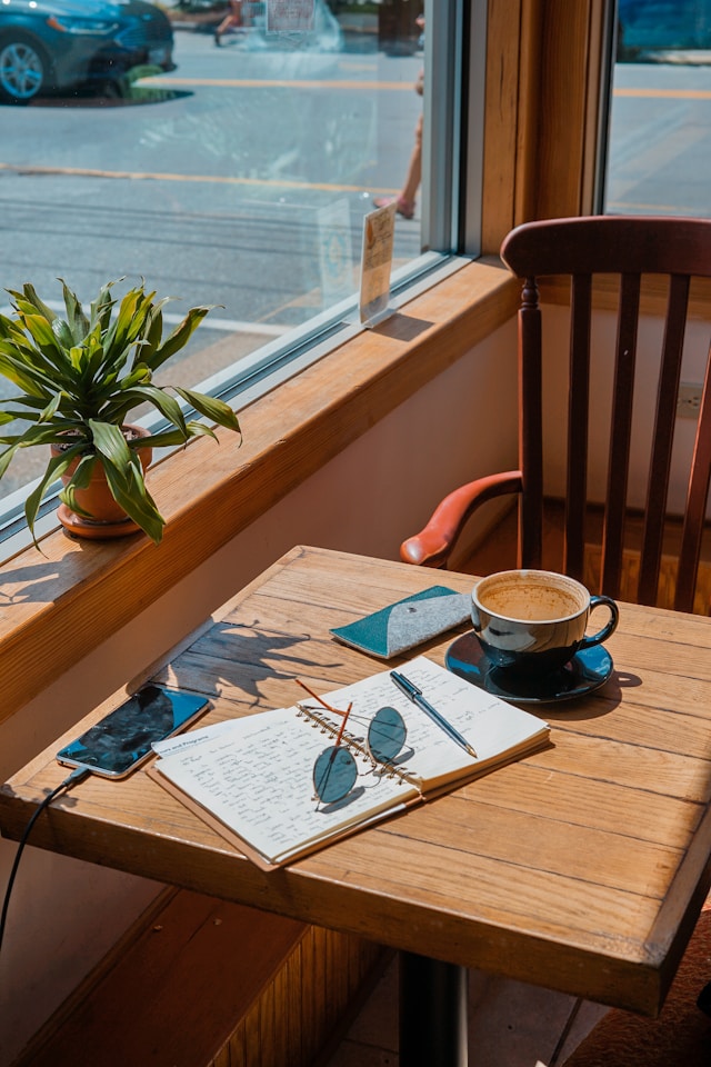 A notebook, a pair of sunglasses, and a coffee sitting on a table. 