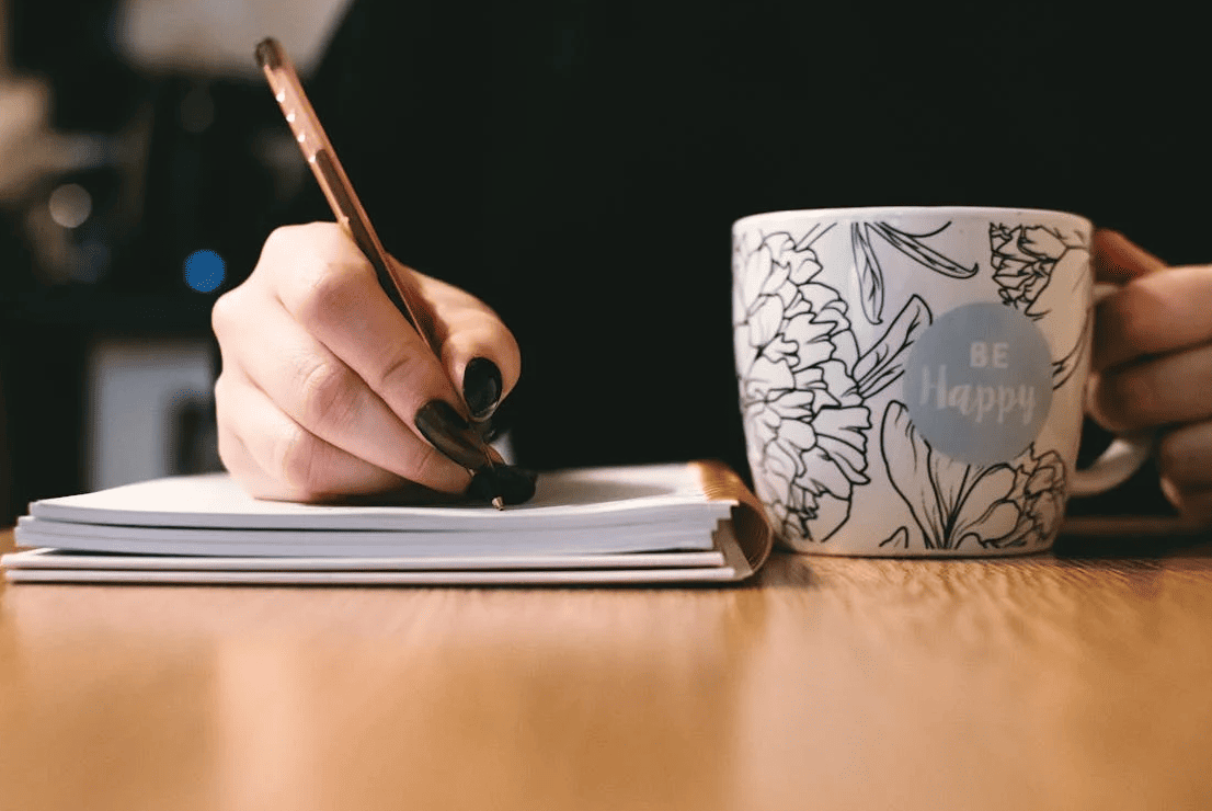 A woman taking notes while holding a mug that says "be happy"