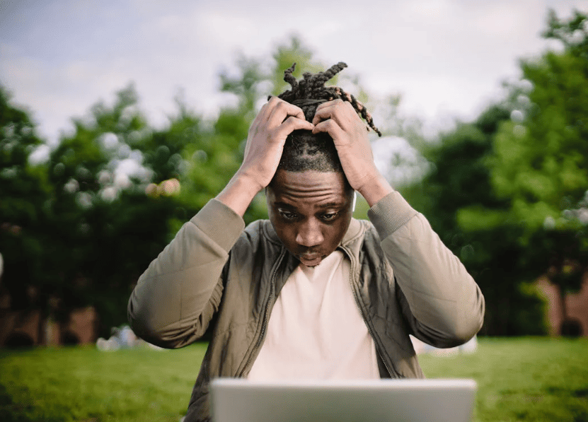 A man holding his head in frustration while looking at his laptop.