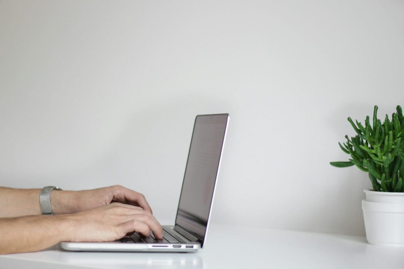 A person typing on a laptop placed on a white desk.