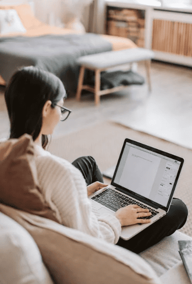 A woman sitting on a sofa and typing on a laptop. 