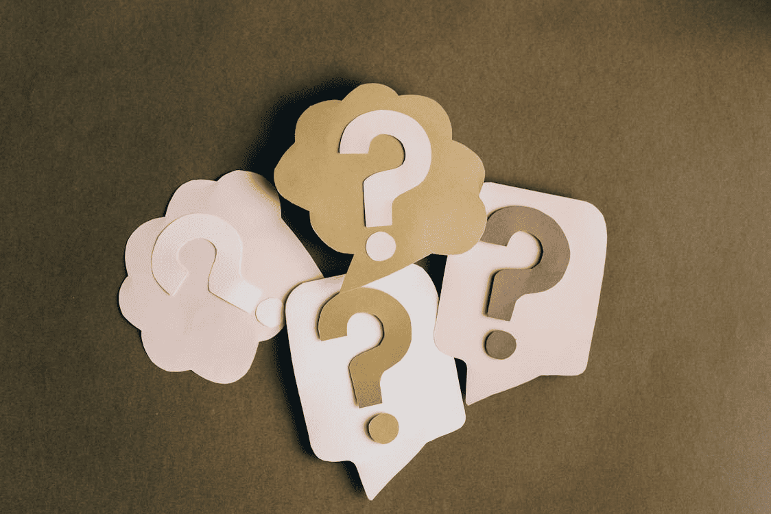 Four pink and gold question marks made out of paper and placed on a brown surface.