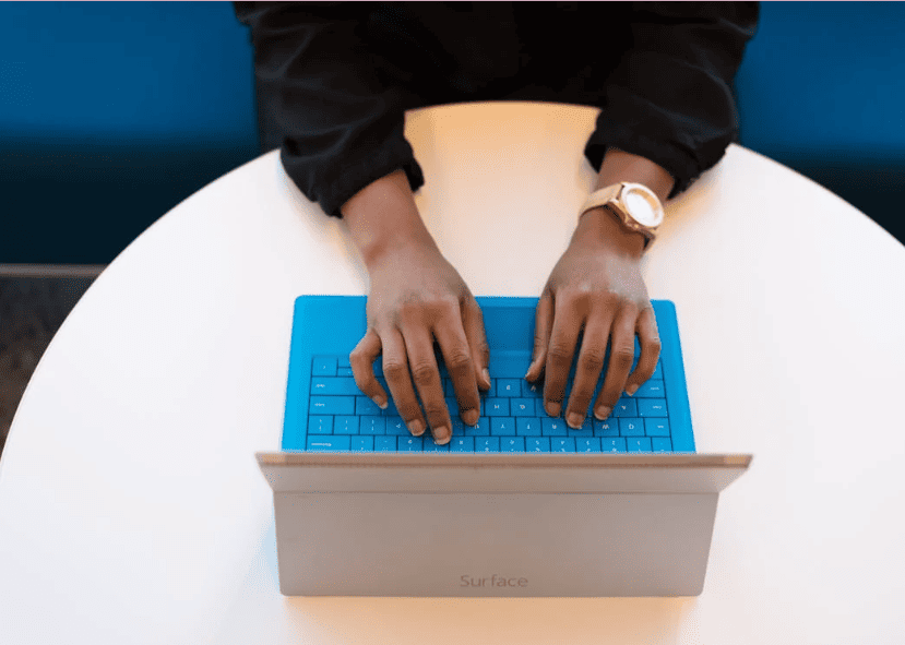 A person typing on a laptop that has a blue keyboard.