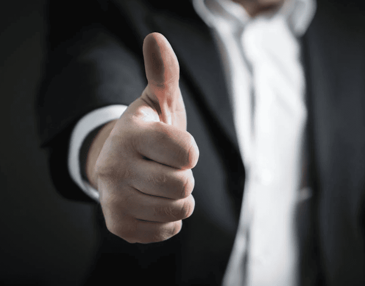 A man in a suit showing the thumbs up sign. 