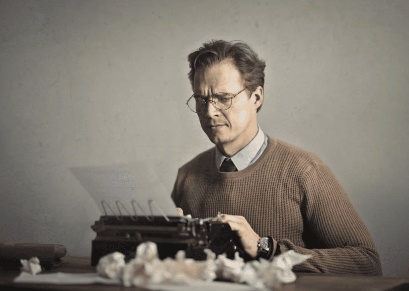 A man with glasses using an old fashioned typewriter. 