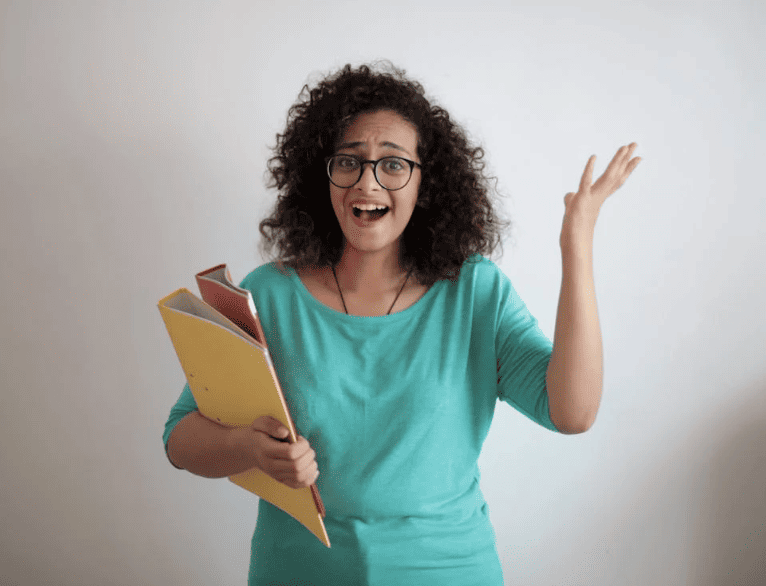 A woman holding a yellow and pink folder and throwing her hands up in the air. 