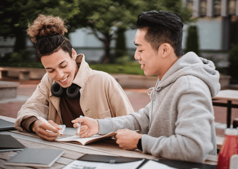 Two college students smiling and pointing at a notebook.