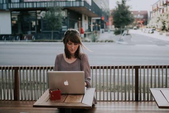 A woman sitting at a table outside typing on her laptop. 