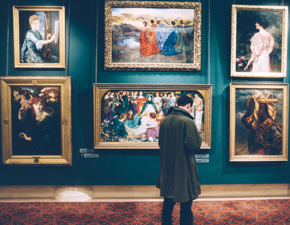 A man standing in front of six paintings in an art gallery.