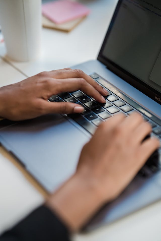 A close up of a person’s hands typing on a laptop. 