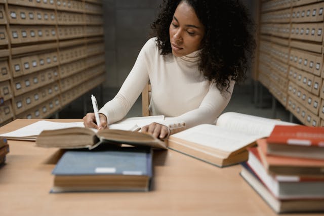 A student writing in a notebook in a library. 