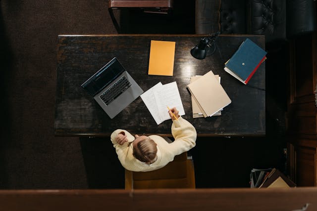 An aerial shot of a person writing an essay at a desk. 