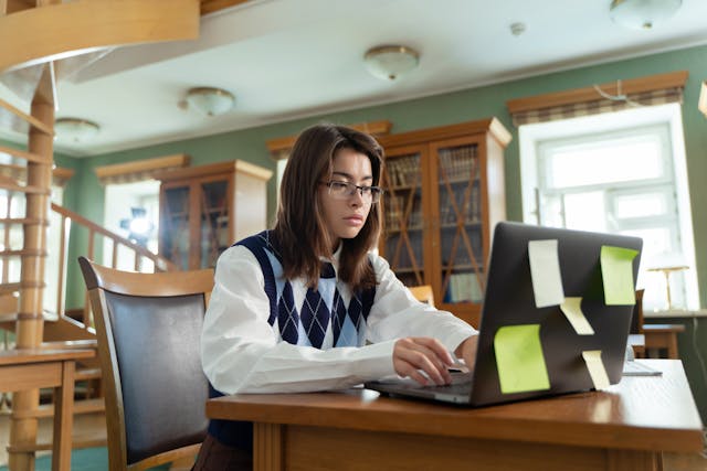 A student in a library working on a laptop. 