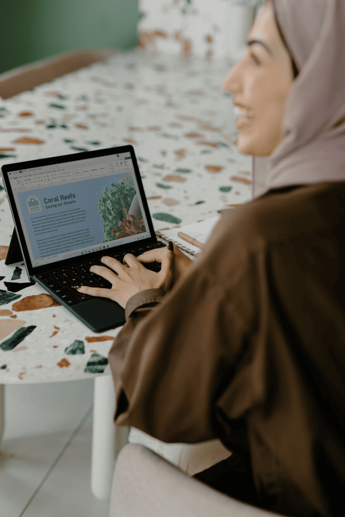 A woman using a laptop on a table and smiling. 