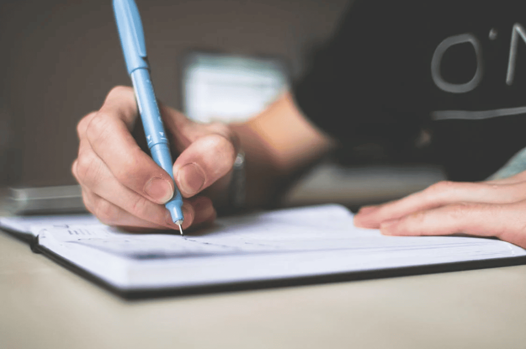 A person writing with a blue pen in a black notebook.