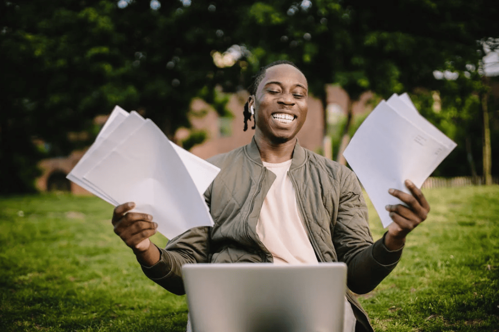 A student with documents in their hands and a laptop smiling.