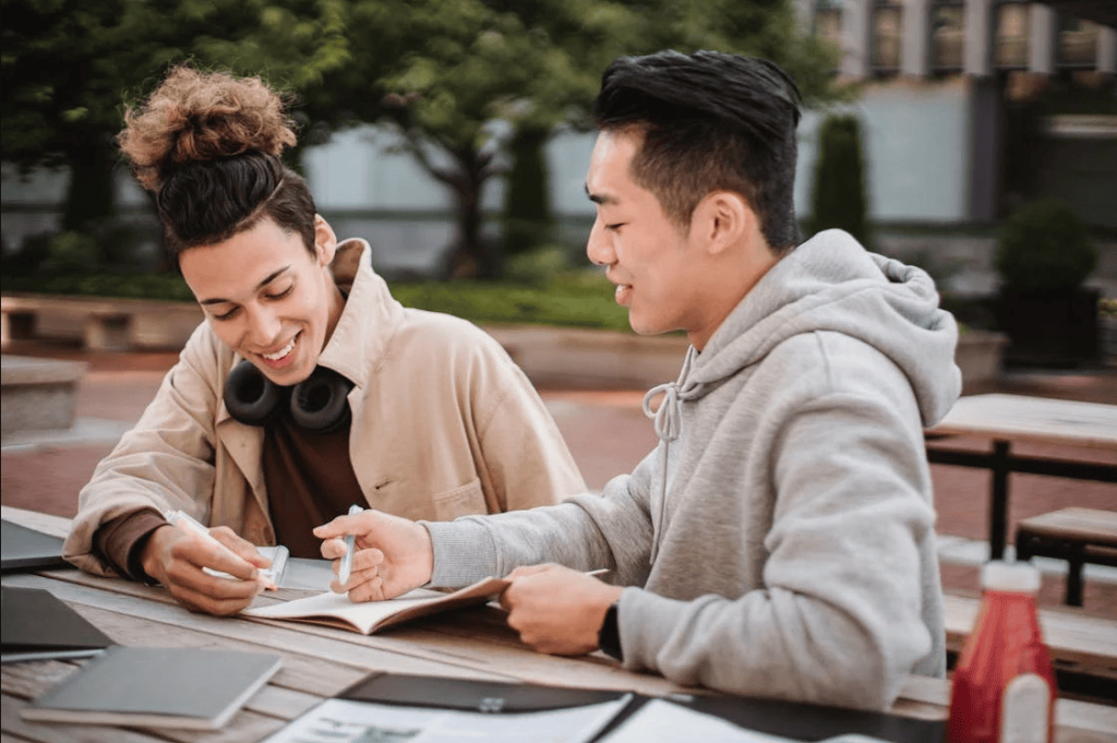 Two men sitting at a wooden table outdoors while working.