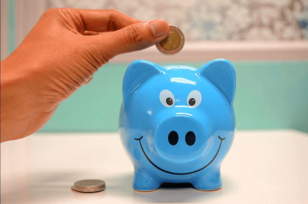 A person putting a coin into a blue piggybank. 