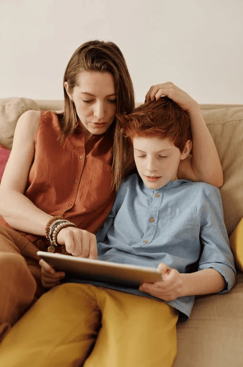 A mother homeschooling a child on a tablet.